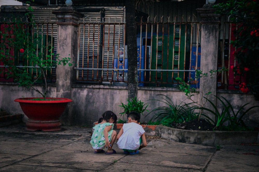 two children sitting on the ground in front of a building