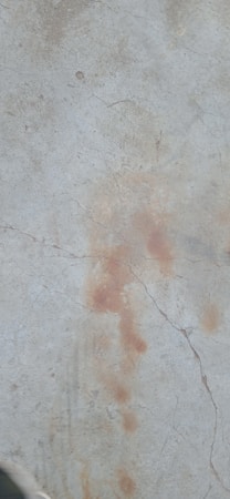A cracked concrete surface with patches of discoloration and stains.
