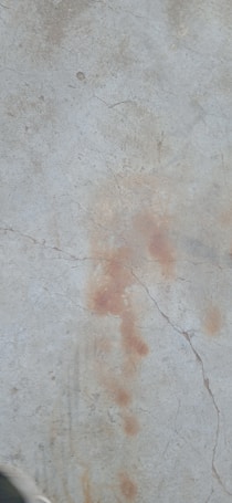 A cracked concrete surface with patches of discoloration and stains.