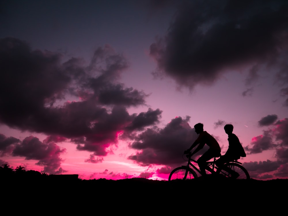 a couple of people riding bikes at sunset