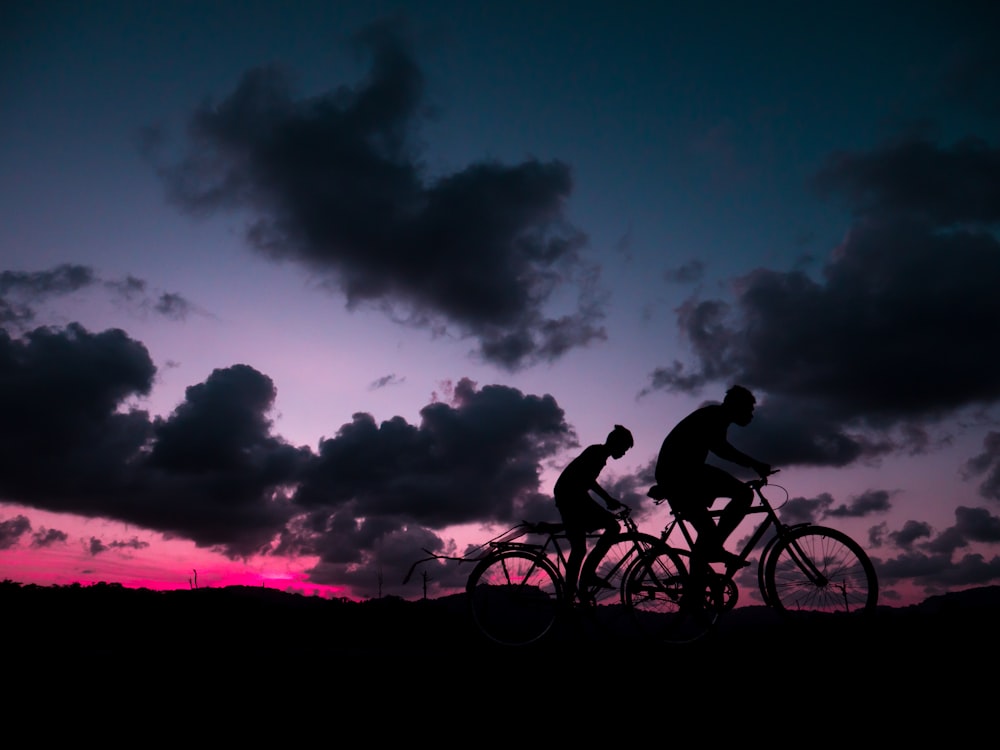 a couple of people riding bikes at sunset