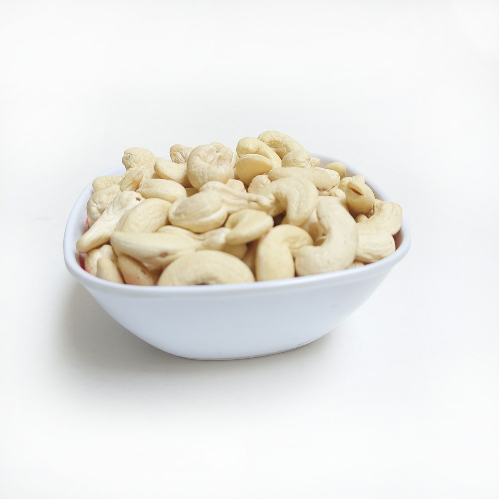 a white bowl filled with cashews on a white surface