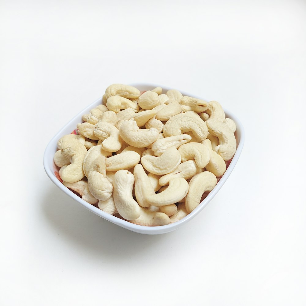 a white bowl filled with cashews on a white surface