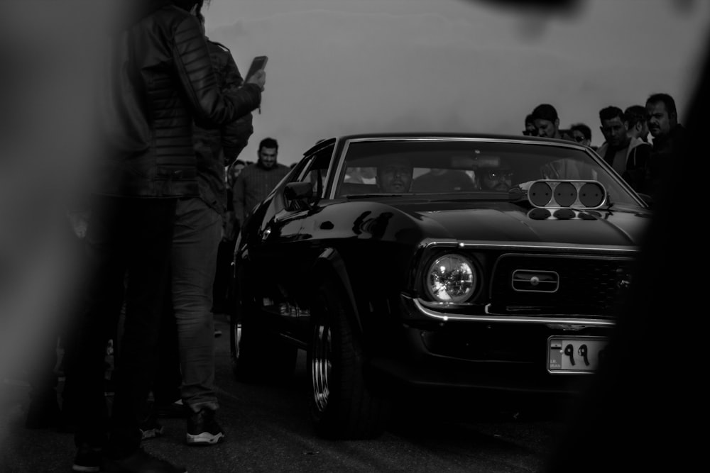 a black and white photo of a man standing next to a car