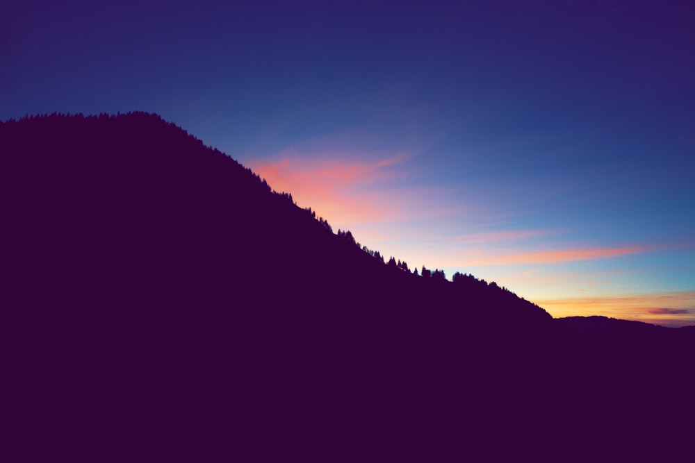 the sun is setting over a mountain with trees