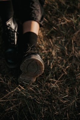 Close-up of a rugged hiking boot resting on a bed of green grass with wood accents in the background.