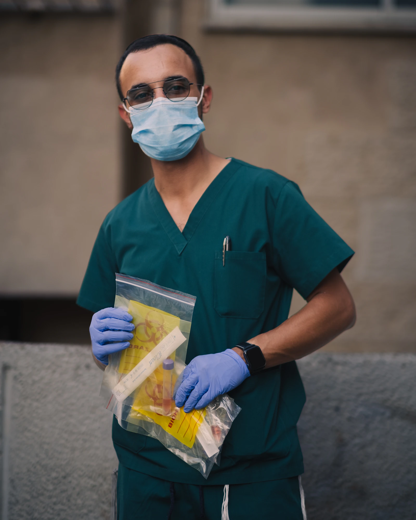 Healthcare professional in scrubs and gloves holding a sealed biohazard specimen bag