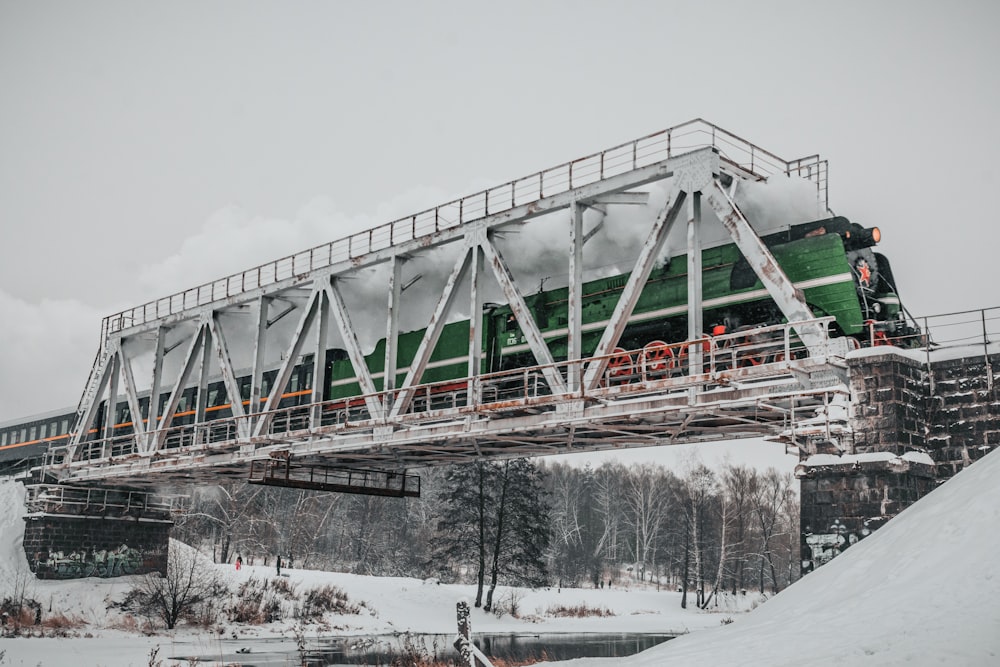 a green train traveling over a snow covered bridge