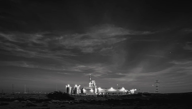 A high-contrast nighttime shot of a landfill gas facility illuminated with green and copper lights against a graphite-black sky.