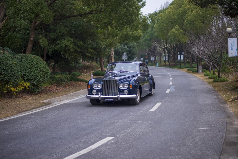 a classic car driving down a tree lined road