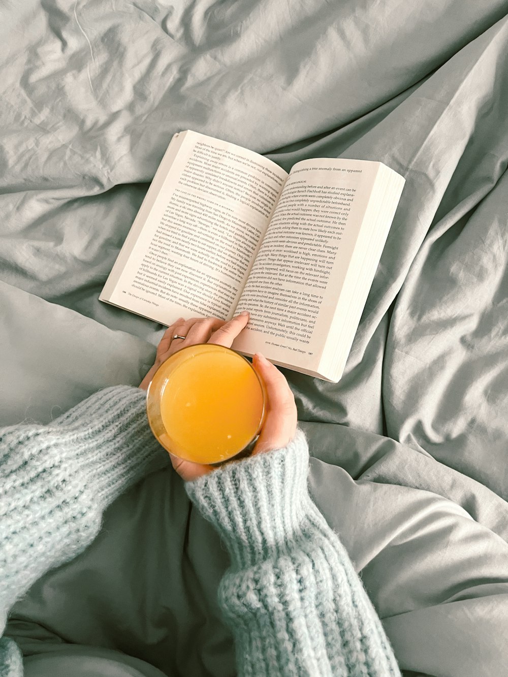 a person laying on a bed with a book and a glass of orange juice