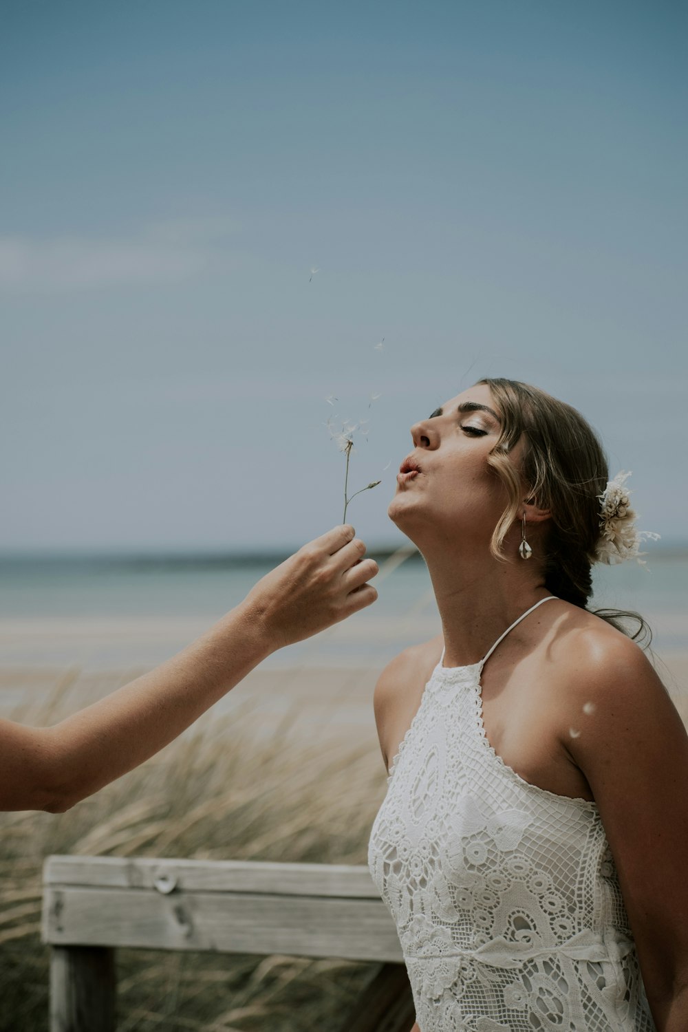 a woman blowing a dandelion on the beach