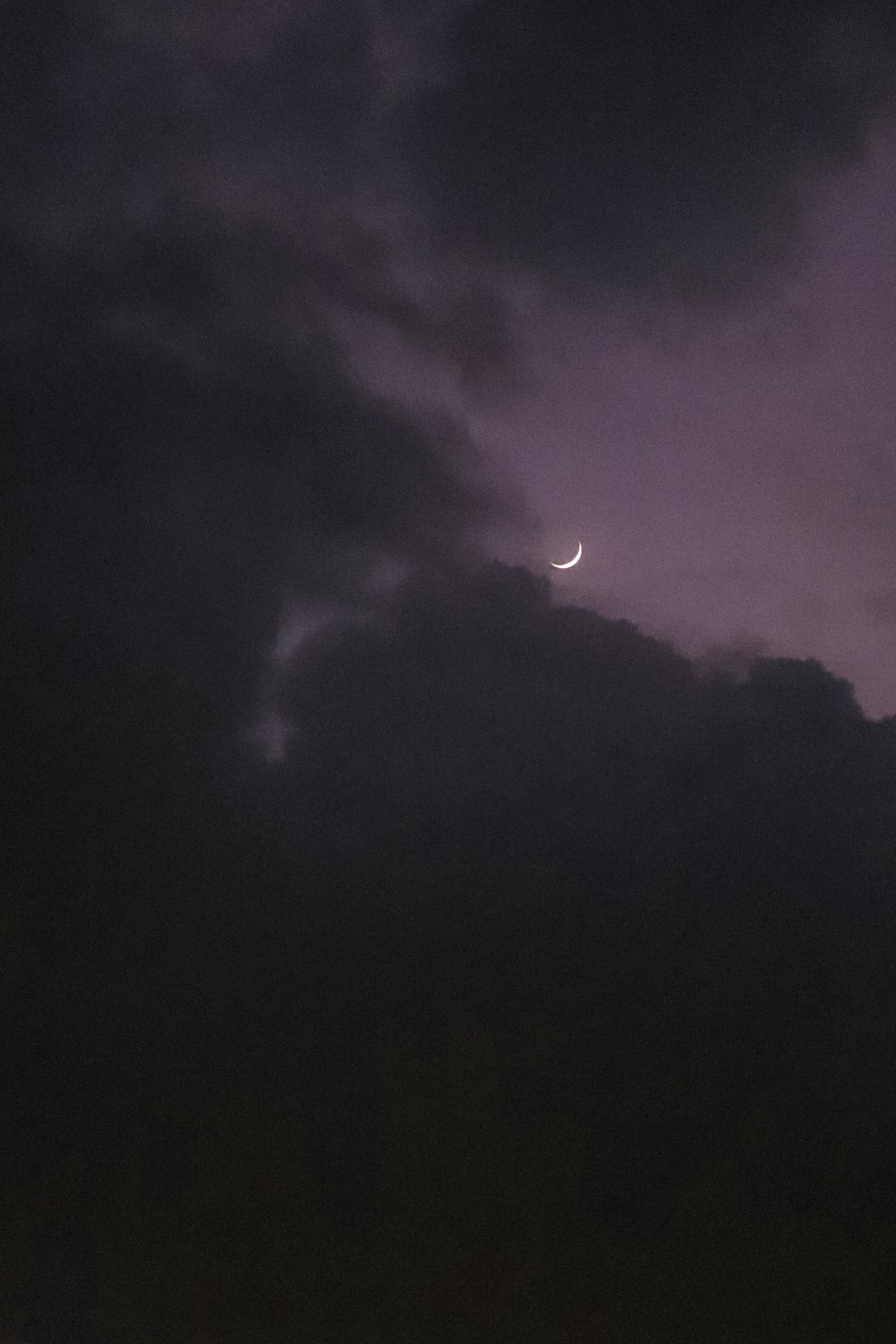 a dark sky with a half moon in the distance