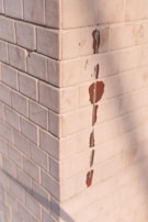 A corner of a tiled wall with white square tiles. Some of the tiles are chipped, revealing a red underlayer.
