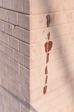 A corner of a tiled wall with white square tiles. Some of the tiles are chipped, revealing a red underlayer.