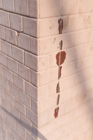 A corner of a tiled wall with white square tiles. Some of the tiles are chipped, revealing a red underlayer.