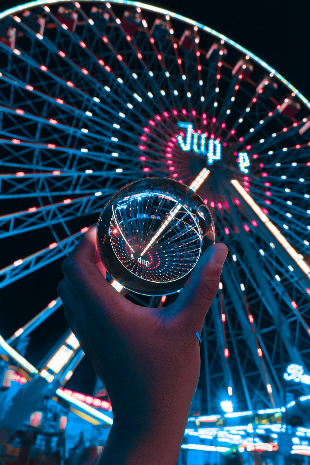 a person holding a glass ball in front of a ferris wheel