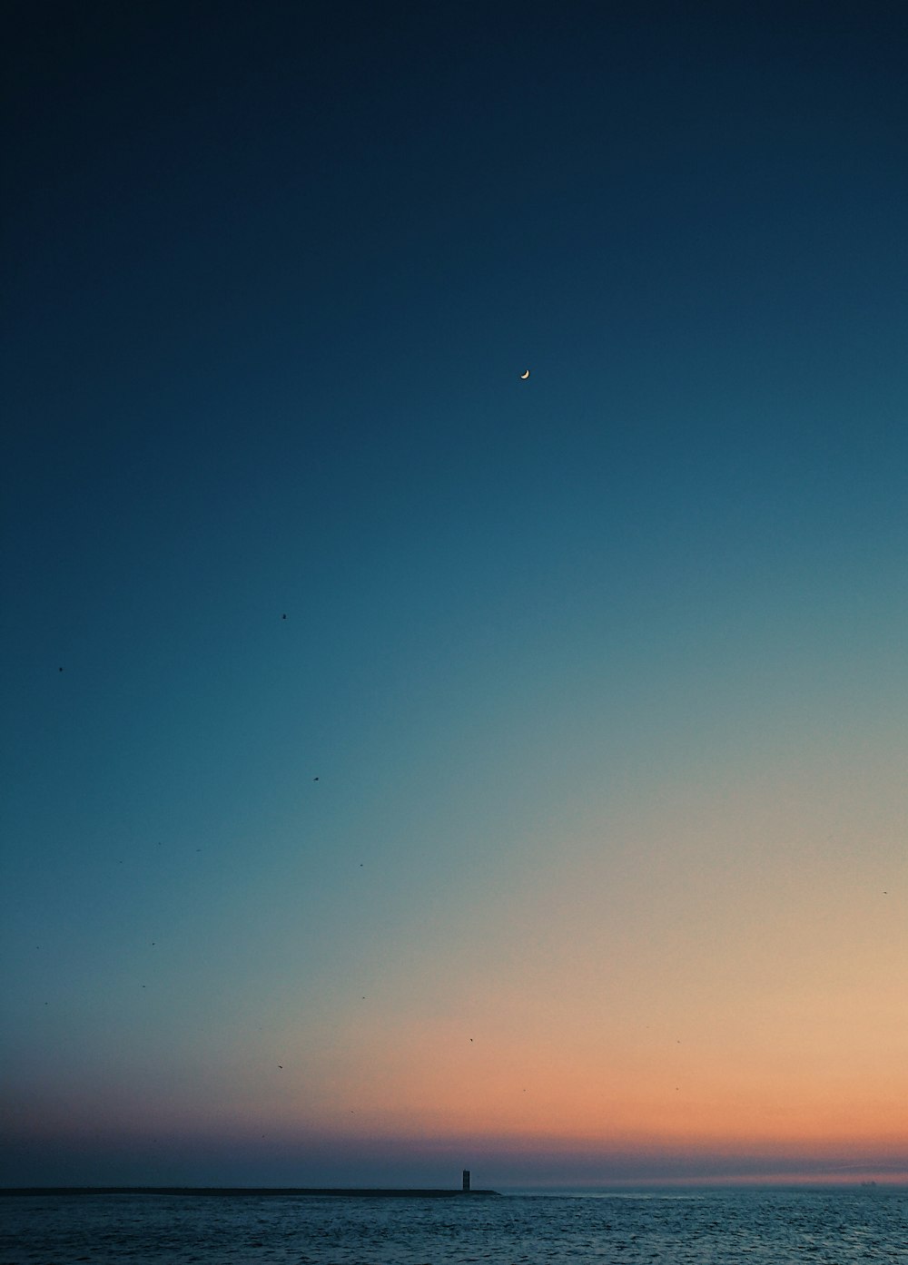 the sun is setting over the ocean with a sailboat in the distance