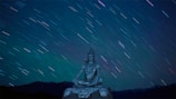A serene figure meditating beneath a starry sky with shimmering constellations.