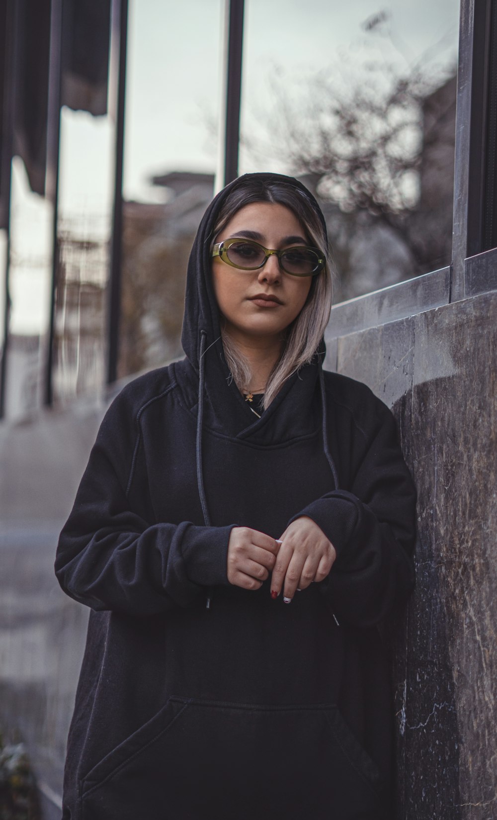 a woman in a black hoodie leaning against a wall