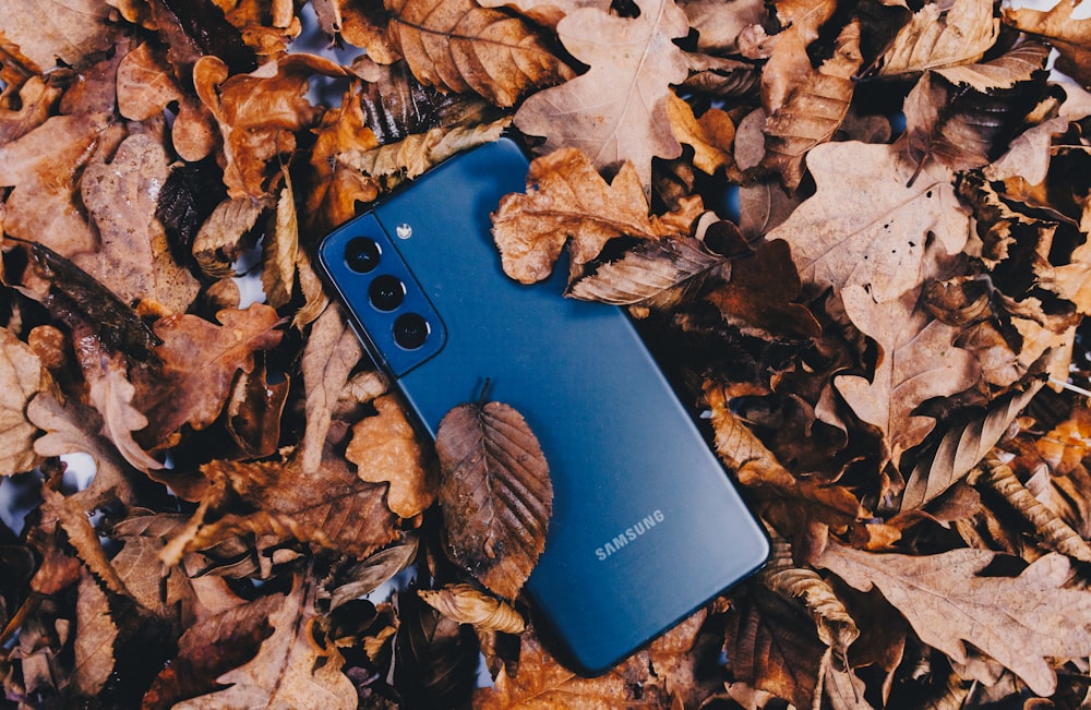 a samsung phone laying on top of a pile of leaves