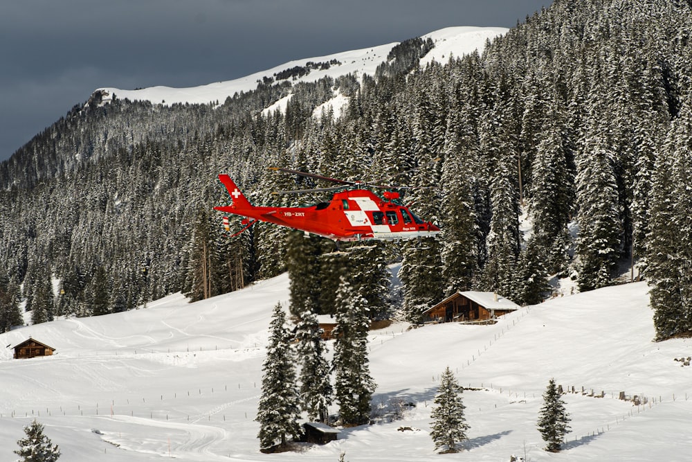 a red helicopter flying over a snow covered mountain