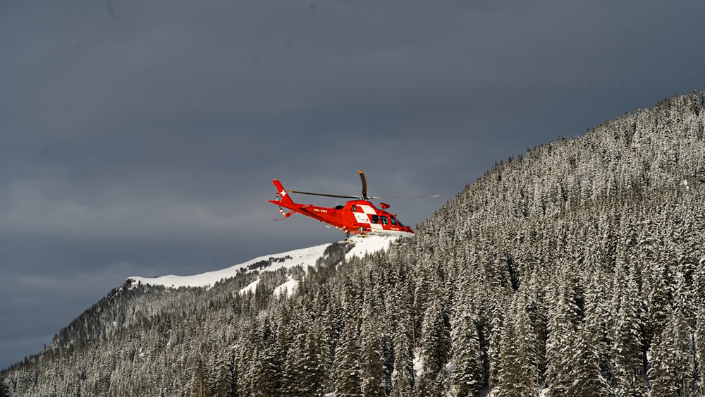 a red helicopter flying over a snow covered mountain