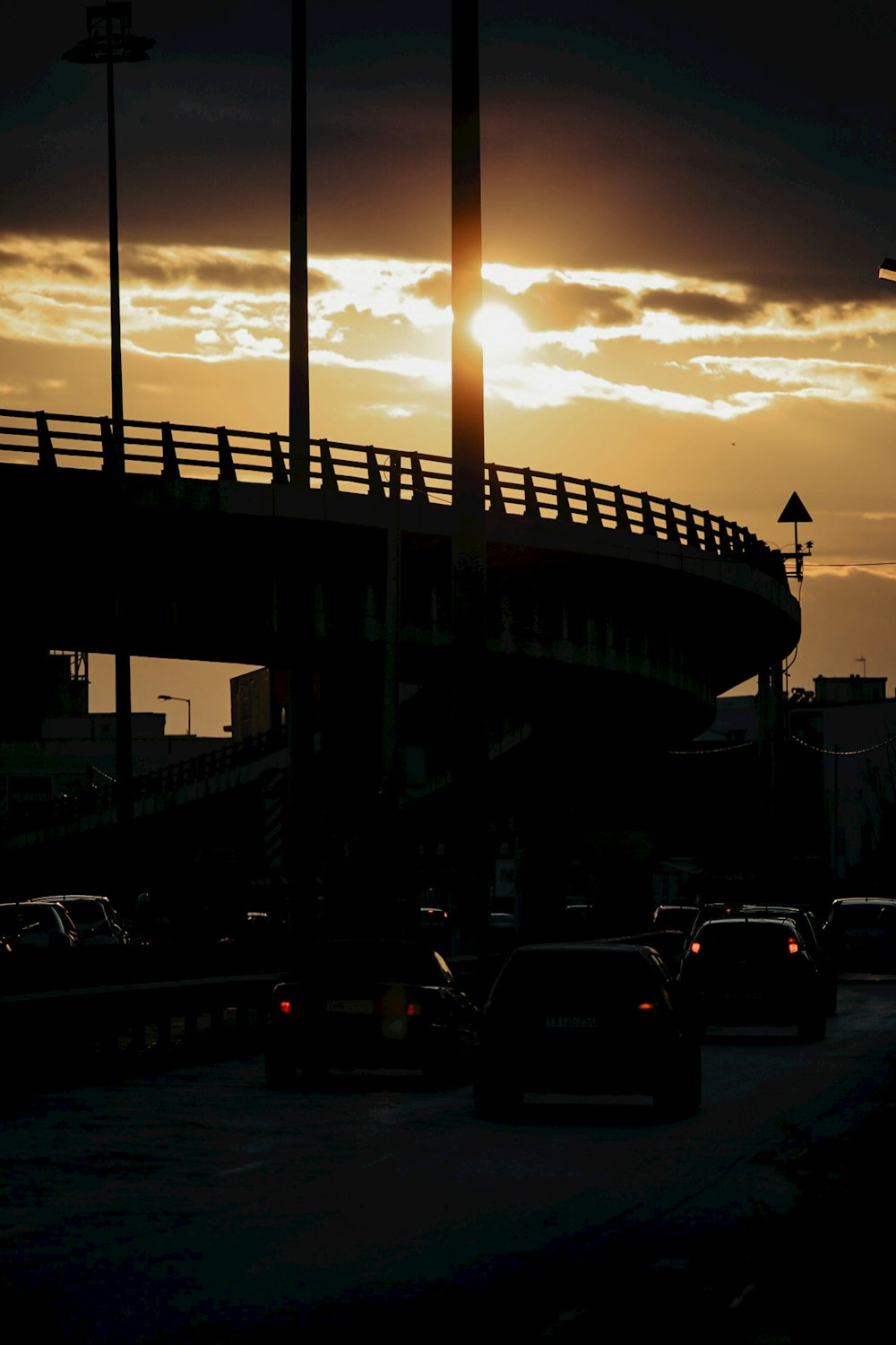 the sun is setting behind a bridge over a highway