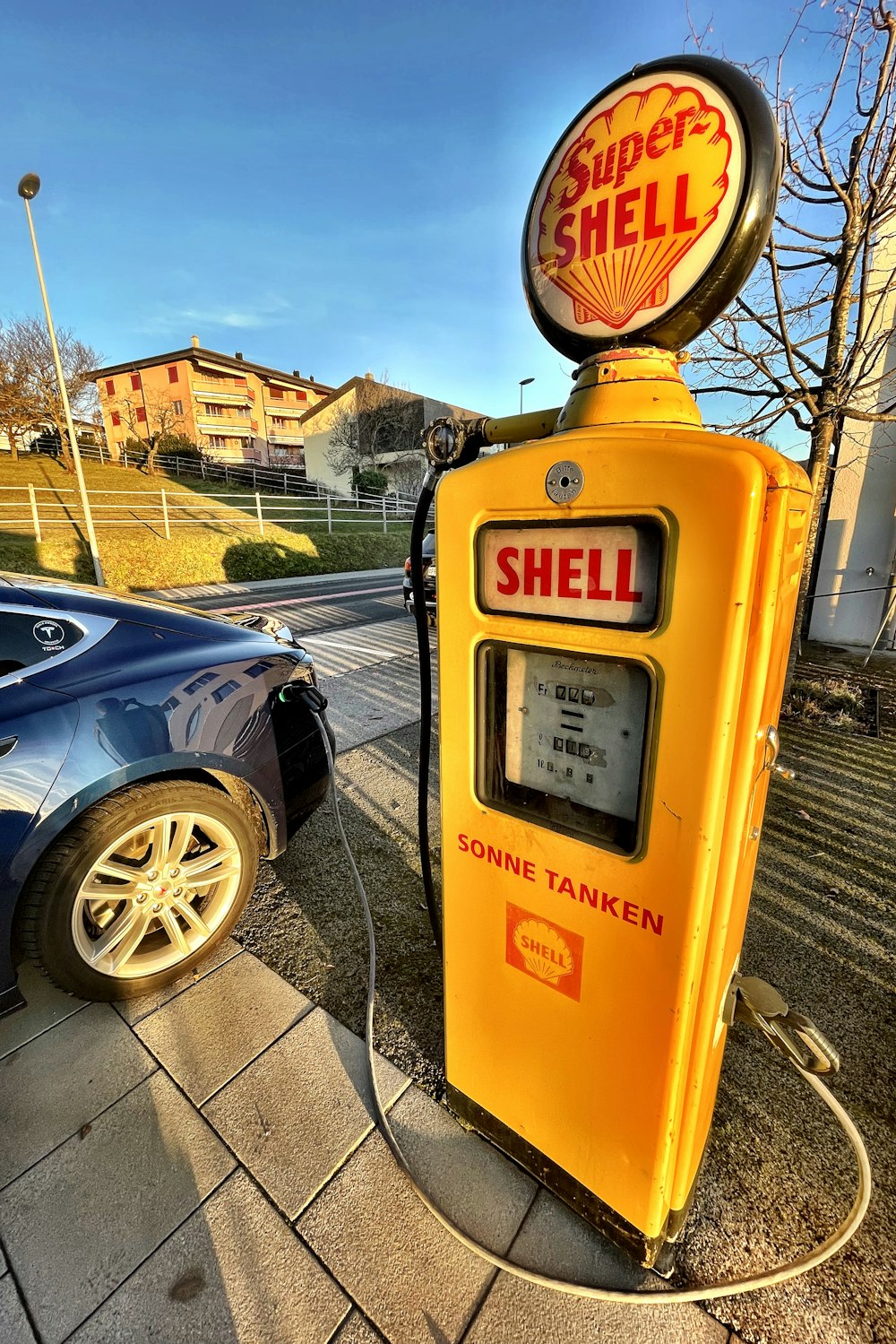 a yellow shell gas pump next to a blue car