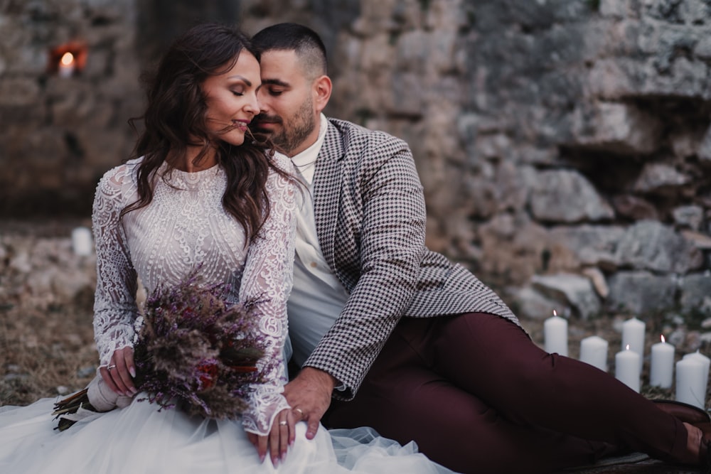 a bride and groom sitting on the ground in front of candles