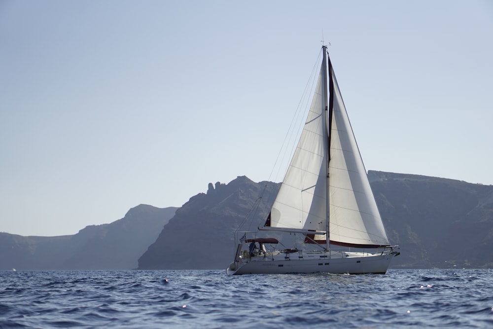 a sailboat sailing in the ocean with mountains in the background