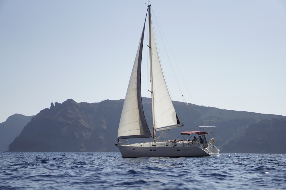 a sailboat sailing in the ocean with a mountain in the background