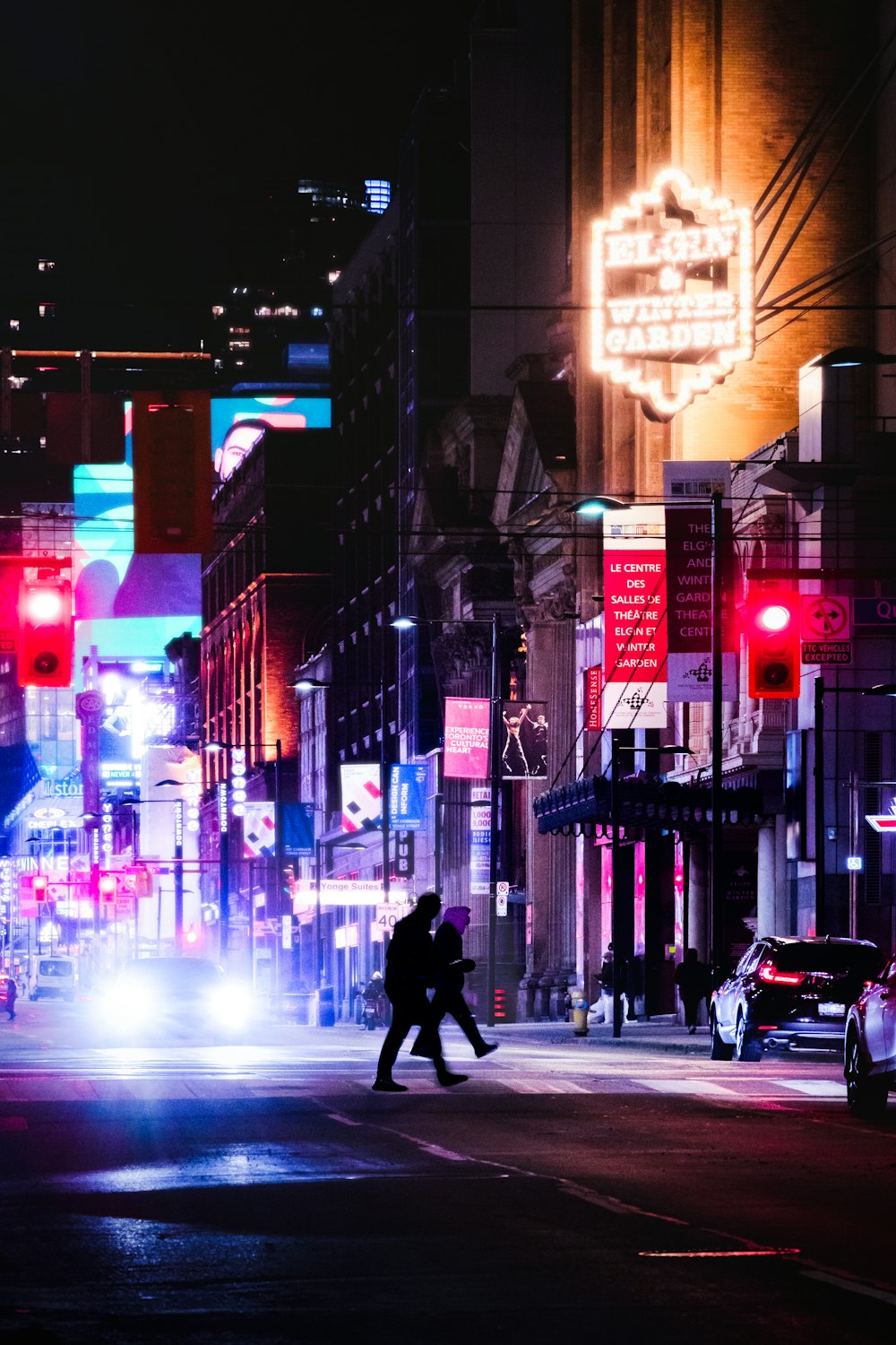 a couple of people crossing a street at night