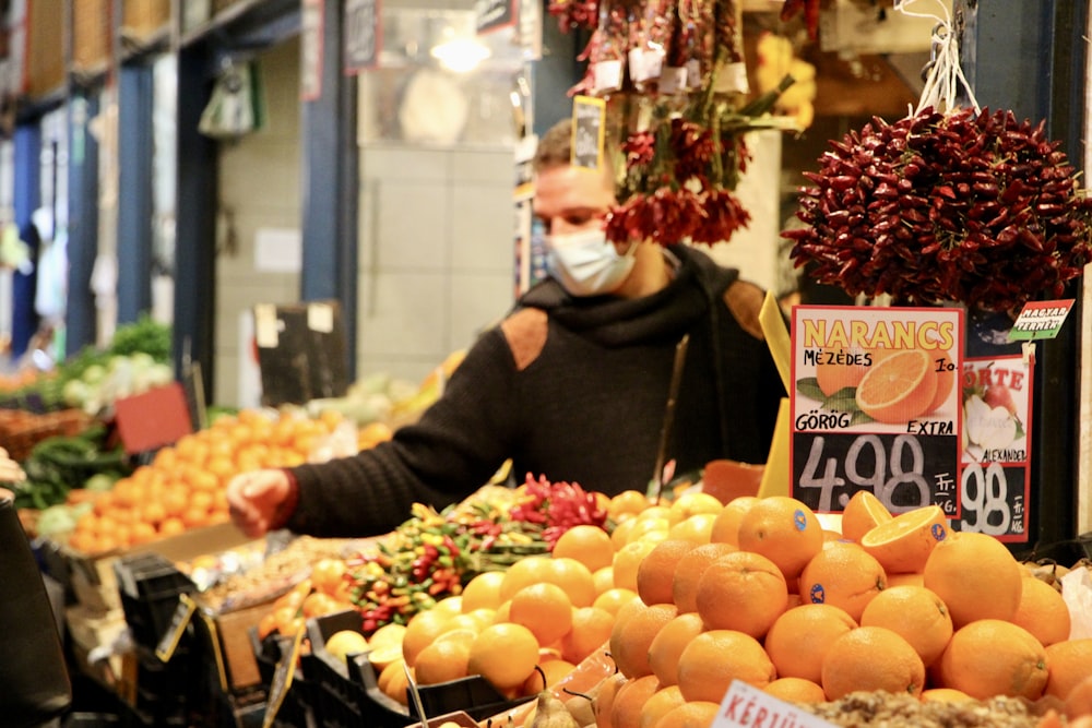 a man wearing a face mask standing in front of a fruit stand