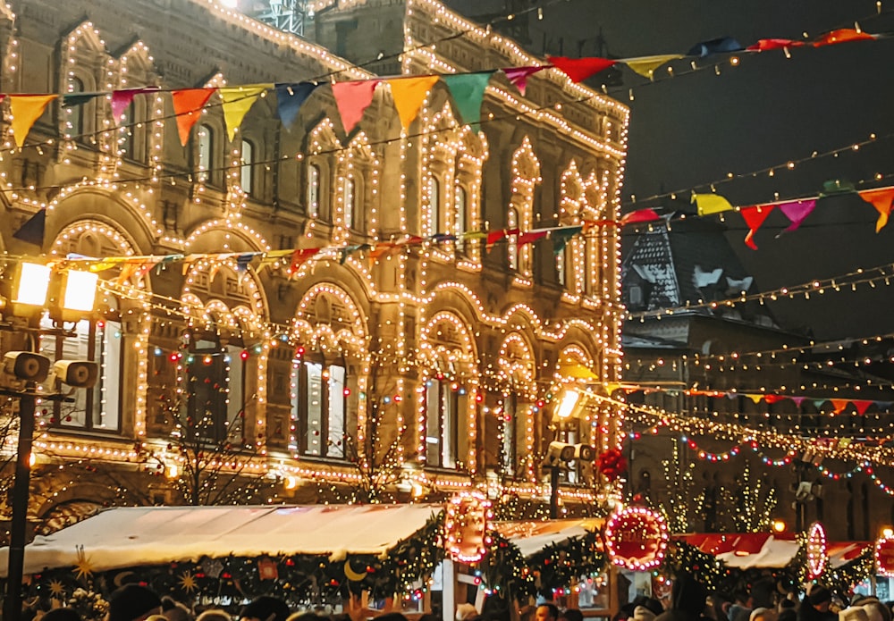 a crowd of people standing around a building covered in christmas lights