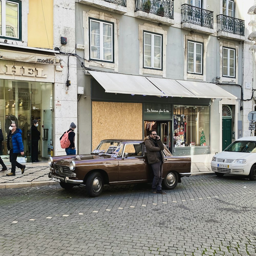 a man standing next to a brown car on a street