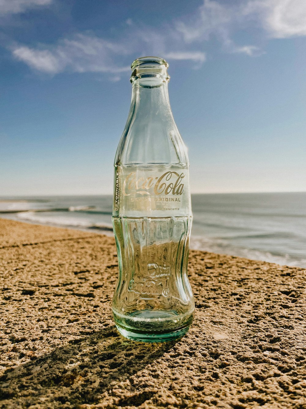 a glass bottle sitting on top of a sandy beach