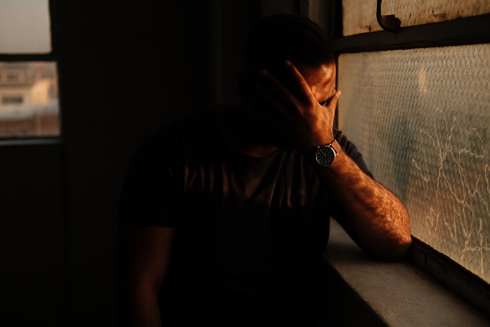 a man sitting in a window sill with his hand on his face