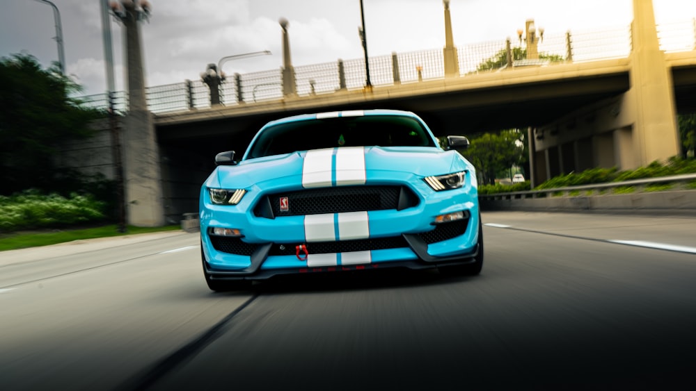 a blue and white mustang driving down a road