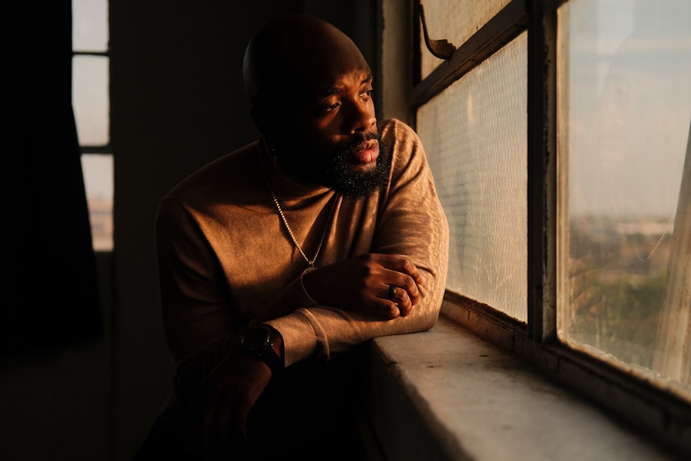 a man sitting on a window sill looking out the window