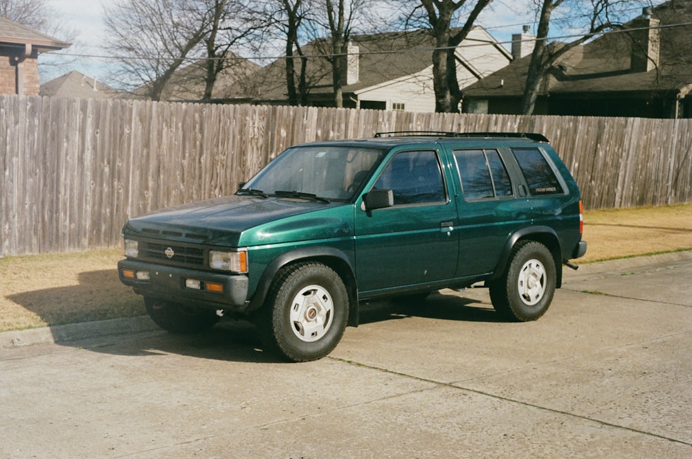 a green suv parked in front of a wooden fence