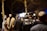 A group of people stands in an outdoor setting, with a uniformed officer in focus wearing a vest labeled 'Gendarmerie'. The scene is dimly lit and the background is blurred, suggesting a night-time or evening environment.
