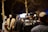 A group of people stands in an outdoor setting, with a uniformed officer in focus wearing a vest labeled 'Gendarmerie'. The scene is dimly lit and the background is blurred, suggesting a night-time or evening environment.