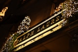 An illuminated store sign displaying 'Ralph Lauren' in elegant gold lettering is surrounded by decorative lights and greenery. The warm glow from the lights creates a luxurious and inviting atmosphere.