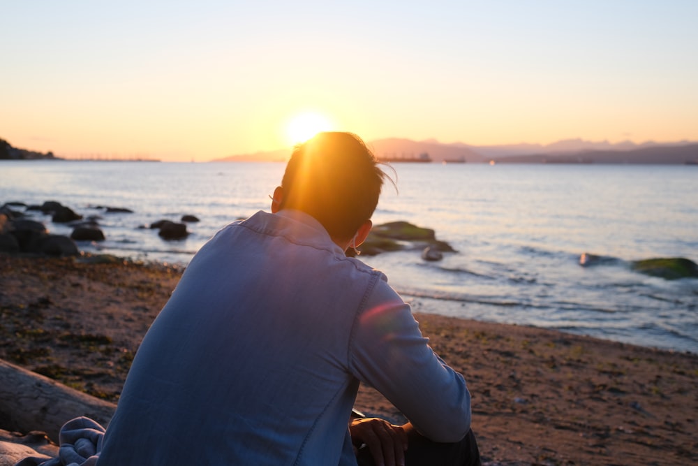 a man sitting on the beach watching the sun set