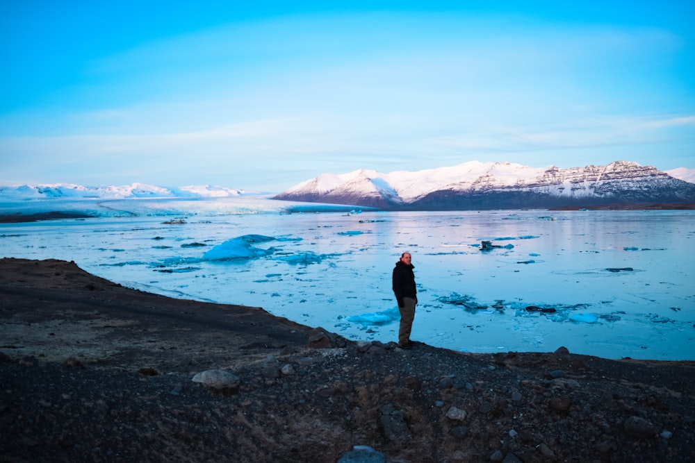 a man standing on top of a rocky beach next to a body of water