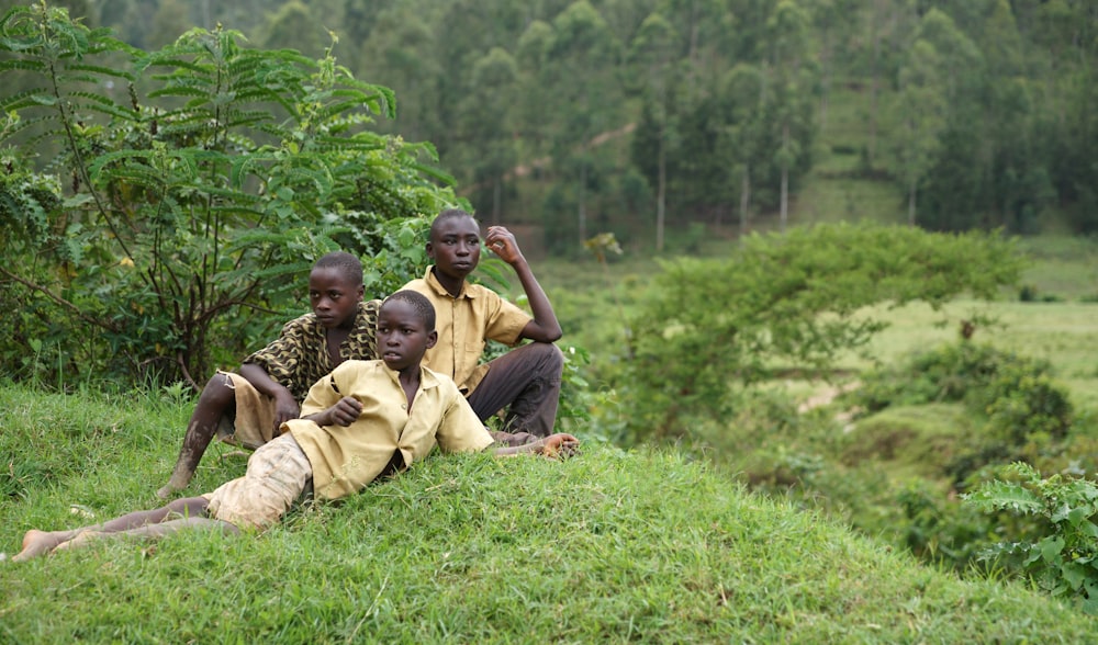a group of young men sitting on top of a lush green hillside