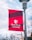 A red and maroon banner with the Stony Brook University logo and name is mounted on a metal pole. The background shows a clear sky with some clouds and tree branches.