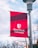 A red and maroon banner with the Stony Brook University logo and name is mounted on a metal pole. The background shows a clear sky with some clouds and tree branches.