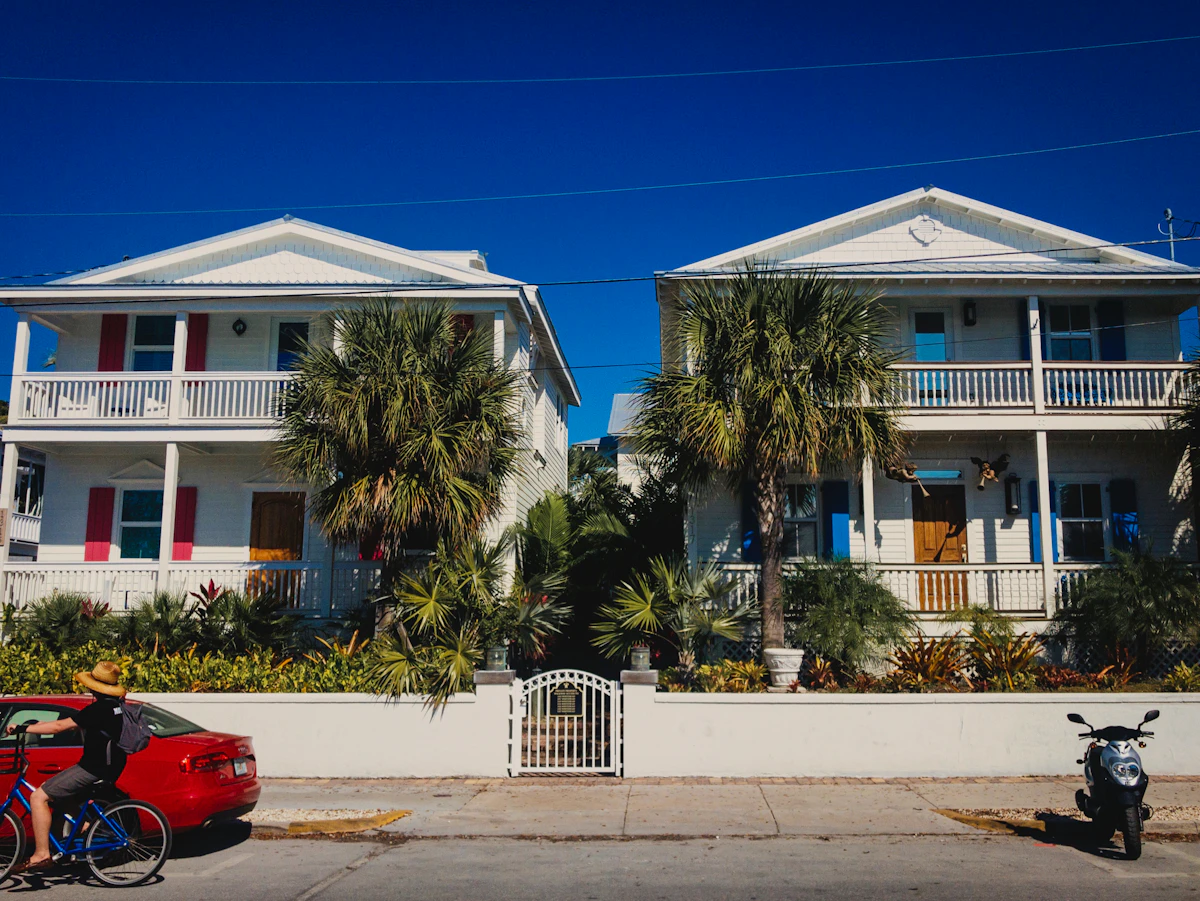 Pastel clapboard houses with balconies behind a white wall and palm trees